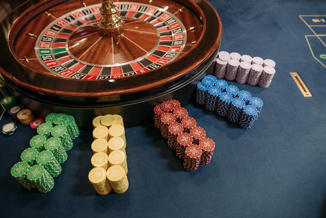 About Vibrant poker chips stacked beside a roulette wheel in a casino setting.